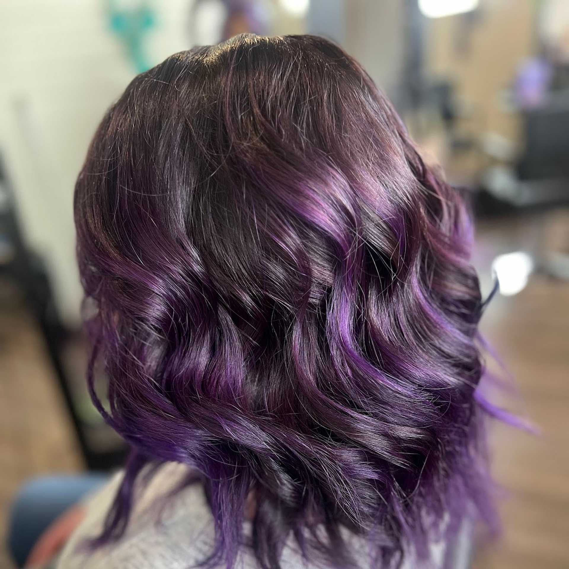 Woman with curly hair featuring a blend of black and vibrant purple highlights.